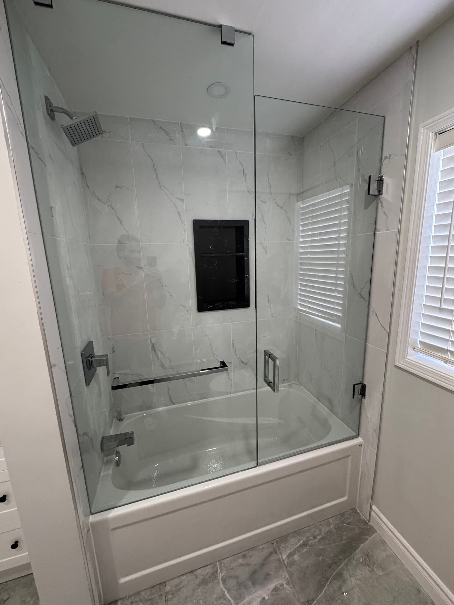 Bathroom renovation Oakville — tub shower combo with frameless glass enclosure and marble tile by Cruzz Construction