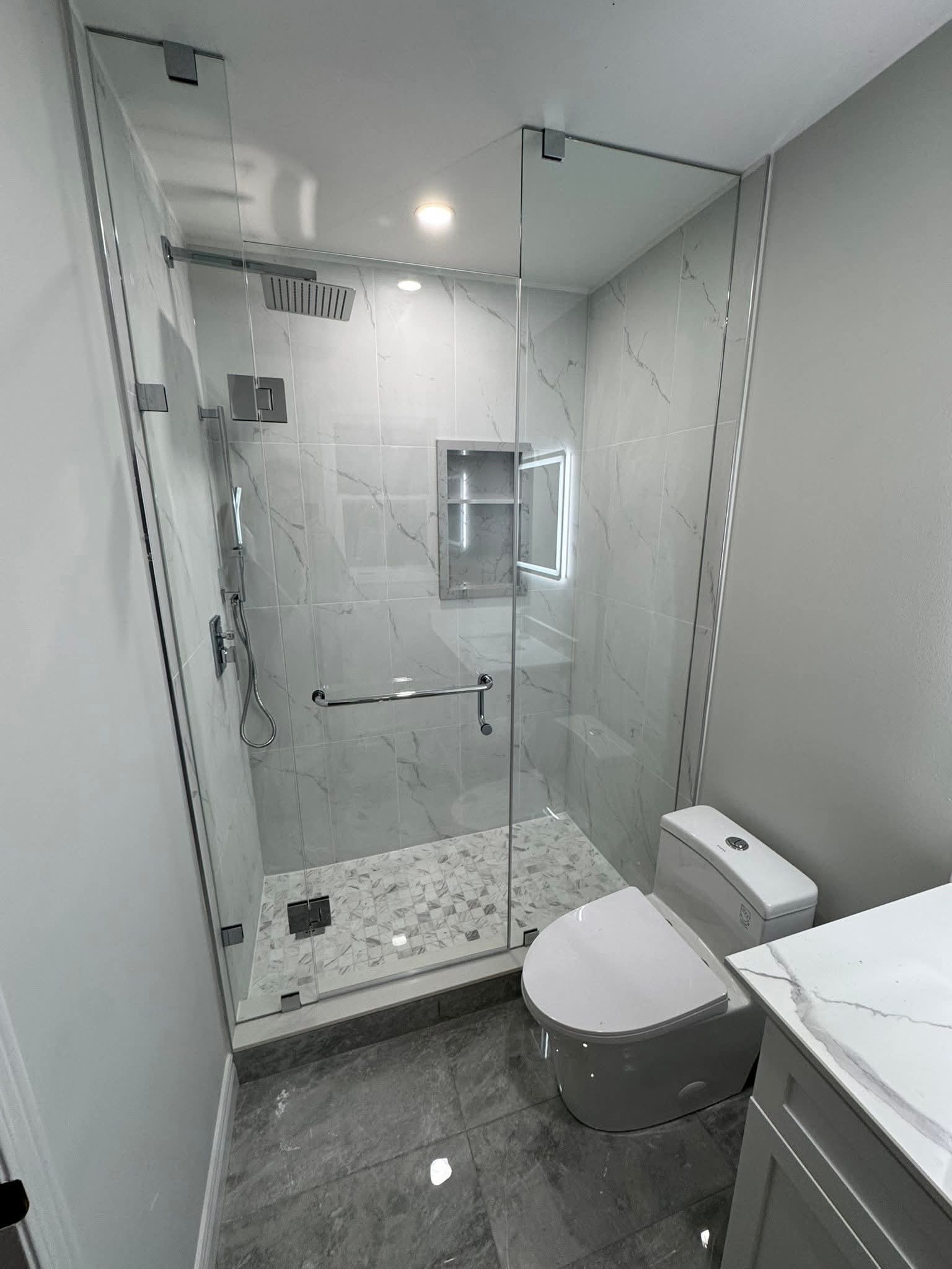 Luxury bathroom renovation Oakville — frameless glass shower with large-format marble tile, rain head, and mosaic floor by Cruzz Construction