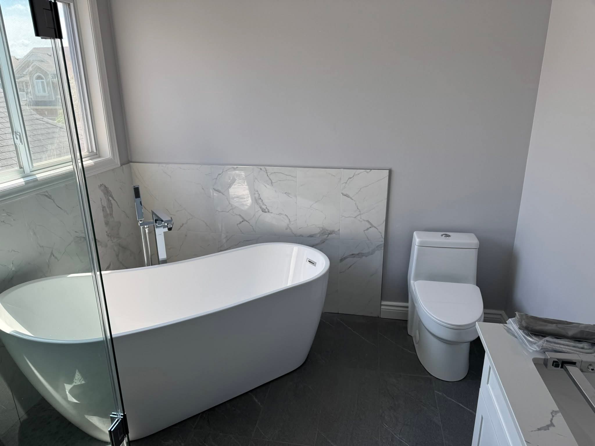 Oakville bathroom renovation — freestanding soaker tub with marble accent wall and floor-mounted filler by Cruzz Construction